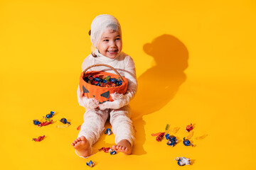 Child in mummy costume holds basket in the form of pumpkin with sweets in his hands