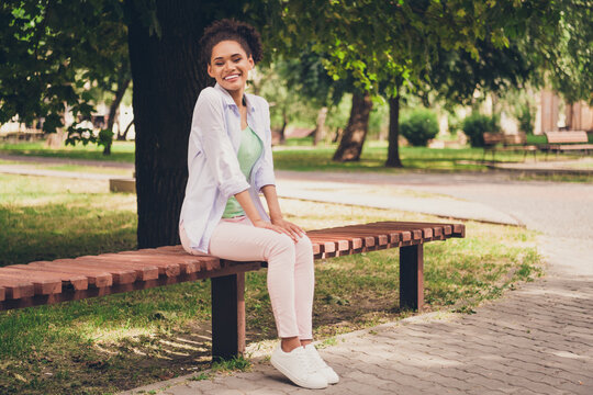 Full body photo of cheerful happy positive afro american woman smile sit bench weekend outside outdoors park