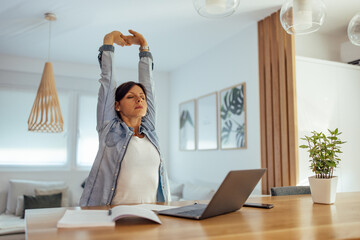 Exhausted woman stretching arms while working overtime.