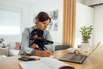 Serious woman working overtime at home, with dog in her lap.