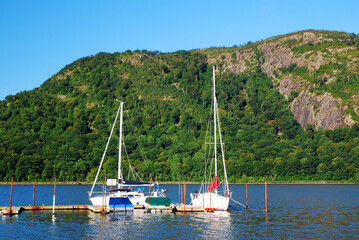 Boats are docked in a small marina surrounded by green hills
