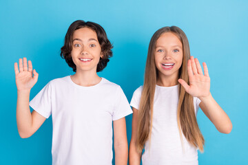 Photo portrait schoolboy schoolgirl waving hands greeting friends isolated pastel blue color...