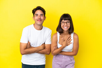 Young mixed race couple isolated on yellow background keeping the arms crossed while smiling