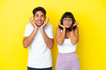 Young mixed race couple isolated on yellow background covering both ears with hands