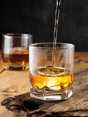 Two glasses with ice cube and whiskey on an old wooden table. Copy space.