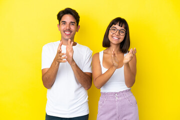 Young mixed race couple isolated on yellow background applauding after presentation in a conference