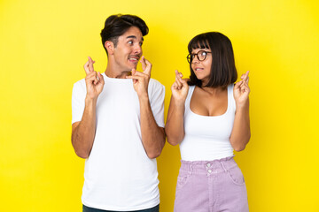 Young mixed race couple isolated on yellow background with fingers crossing and wishing the best