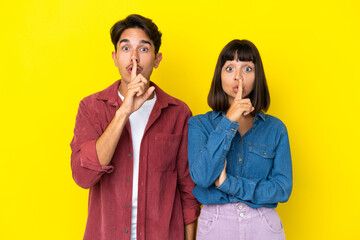 Young mixed race couple isolated on yellow background showing a sign of silence gesture putting finger in mouth