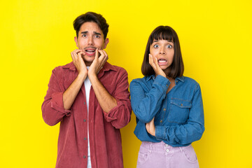 Young mixed race couple isolated on yellow background surprised and shocked while looking right