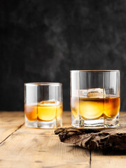 Two glasses with ice cube and whiskey on an old wooden table. Copy space.