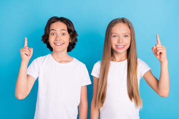 Photo of two genius kids have idea raise fingers show empty space wear white t-shirt isolated blue...