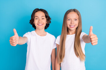 Photo of two reliable children raise two thumbs up approve tips wear white t-shirt isolated blue...