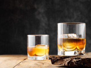 Two glasses with ice cube and whiskey on an old wooden table. Copy space.