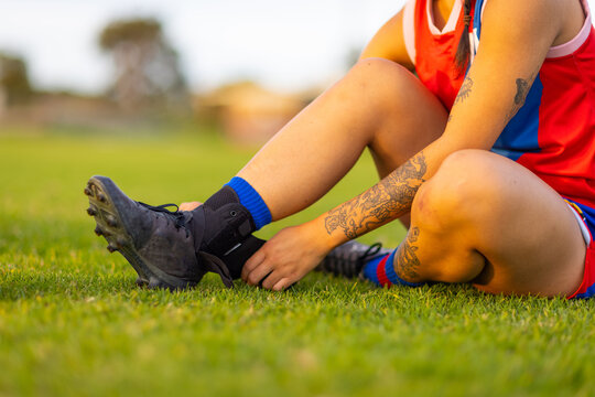 female football player sitting on grass adjusting ankle brace
