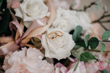 Pink flowers and two golden wedding rings on white background.