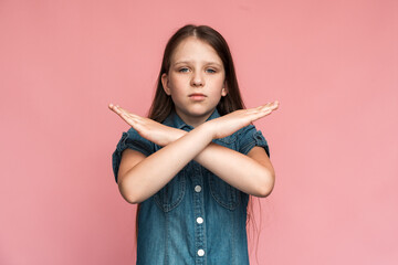 Stop, I'm warning. Portrait of angry determined little girl crossing hands and looking at camera with aggression, showing stop gesture, way prohibited. Indoor studio shot pink background