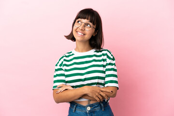 Young mixed race woman isolated on pink background looking up while smiling