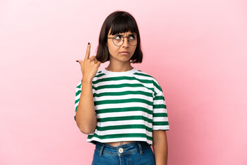 Young mixed race woman isolated on pink background making the gesture of madness putting finger on...
