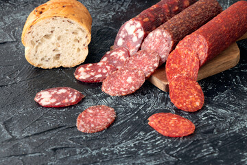 three kind of different sausages on a cutting board near bread. Pieces of sausage cut into circles...