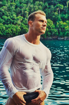 Handsome young bodybuilder by the sea with wet shirt on