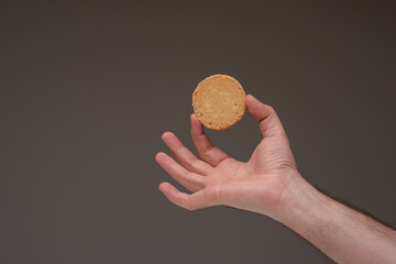 Single shortbread biscuit held by male hand. Close up studio shot, isolated on brown background