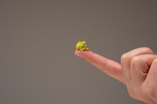 Fresh green Wasabi paste on the pointing fingers of a male hand. Close up studio shot isolated on brown background