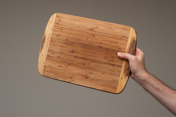 Caucasian male holding a wooden kitchen cutting board. Close up studio shot, isolated on brown background