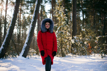 Fototapeta na wymiar a series of photographs with a young woman in the winter forest. girl in a snowy park. in a red jacket. winter walk in nature. Cold season. Beautiful Girl In Red Jacket In Snowy Forest In Winter Day.