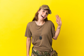 Military caucasian woman with dog tag isolated on yellow background saluting with hand with happy expression