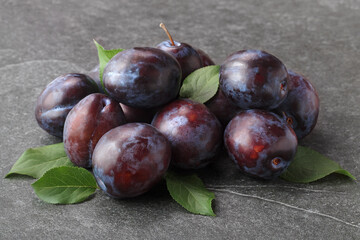 Pile of fresh purple plums with leaves on stone table, selective focus.