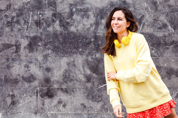 Young brunette woman with yellow outfit laughing over gray background