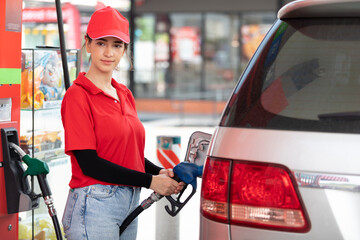 woman worker holding petrol hose and refueling vehicle or car at gas station