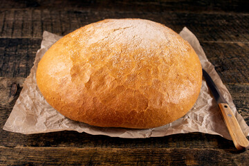 Round rye bread lying on a wooden table.Bread lying on the paper next to an old knife.