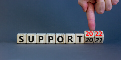 Symbol of planning 2022 support new year. Businessman turns a wooden cube and changes words 'support 2021' to 'support 2022'. Beautiful grey background, copy space. Business, 2022 support concept.
