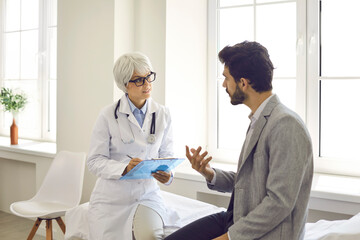 Worried man talking to doctor while sitting in exam room during consultation in modern clinic or hospital. Concerned male patient telling serious physician or general practitioner about his problem