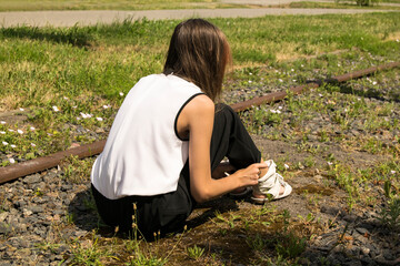Naklejka na ściany i meble A young caucasian girl sits on an old abandoned railway. Back view, summer day.