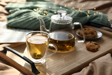 Wooden tray with freshly brewed tea and cookies on bed in room. Cozy home atmosphere