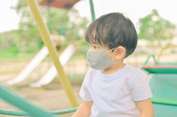 Little boy playing in the playground, the child is wearing a protective mask on the face during the...