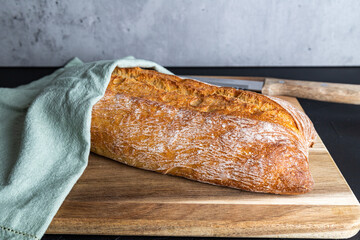 Fresh Italian ciabatta covered with a kitchen towel, lies on the wooden board