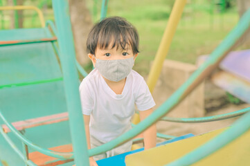 Fototapeta na wymiar Little boy playing in the playground, the child is wearing a protective mask on the face during the quarantine of coronavirus, covid-19, virus protection.