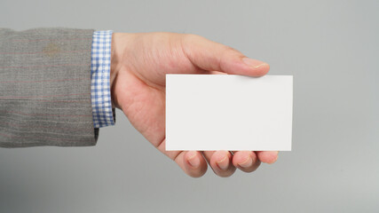 Hand is holding white blank card and wear suit on gray background. business man concept