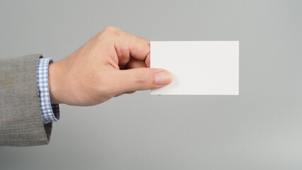 Hand is holding white blank card and wear suit on gray background. business man concept