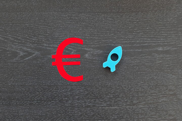 The euro sign is red. a rocket flying up is blue on a dark background. The concept of financial cash growth.