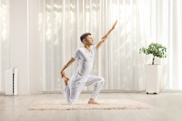 Young man in white clothes practicing yoga on a carpet in a room