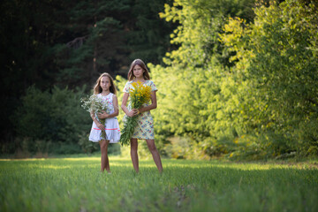 Two girls friends with bouquets of flowers are posing in the forest.