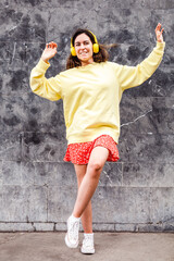 Young brunette woman dancing with a limp. Autumn outfit and headphones