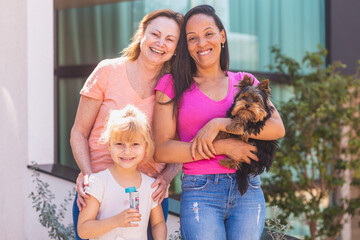 Smiling lesbian couple with child and pet puppy. Lesbian couple holding with their adoptive...