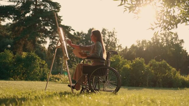 Woman disabled artist in a wheelchair paints a picture in the park. Disabled Person, Woman Artist, Art for Sales, Inspiration in Nature.