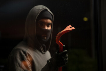 Hooded hooligan in balaclava holding a crowbar, black background