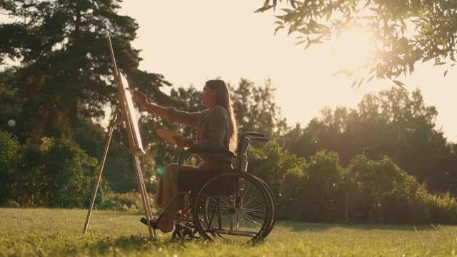 Woman disabled artist in a wheelchair paints a picture in the park. Disabled Person, Woman Artist, Art for Sales, Inspiration in Nature.